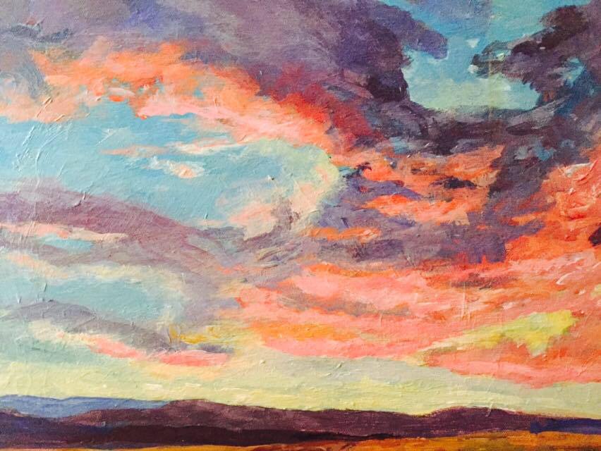 Low-level purple mountains and a ruddy desert appear on a skyline just over a setting sun and underneath a cloud scape of pink, orange, and purple.